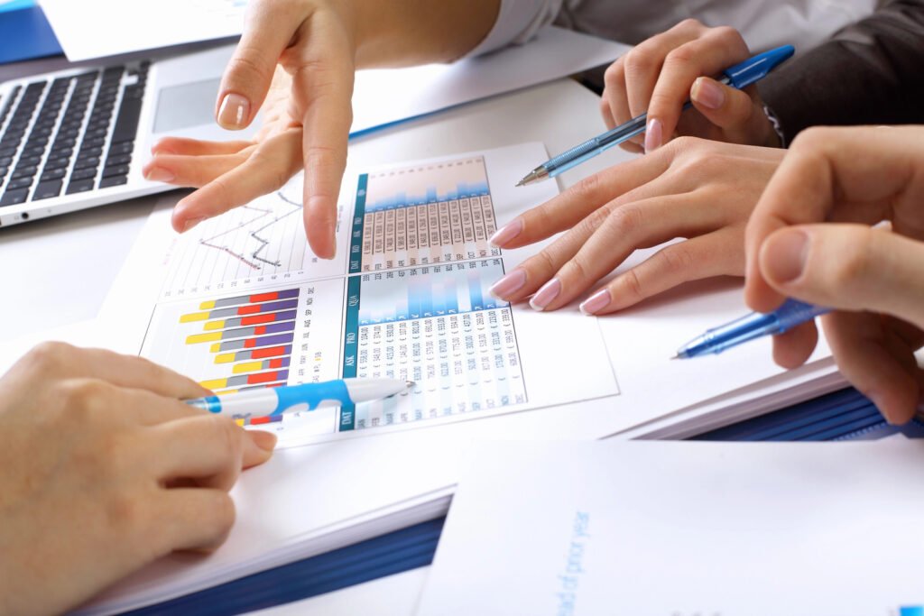 Hands point at charts and graphs on paper, with pens and a laptop nearby, meticulously analyzing data for penetration testing strategies.